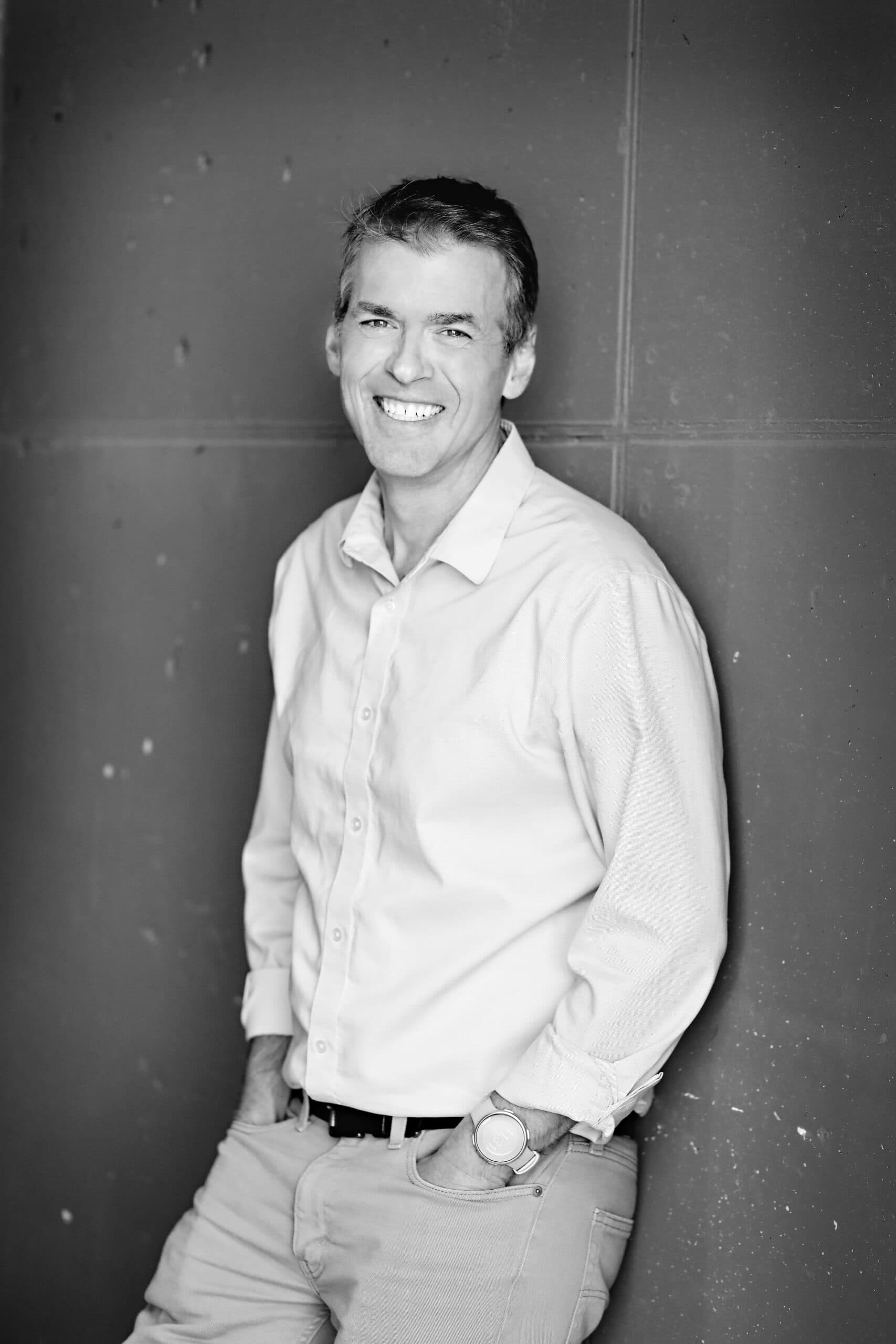 Kevin Williams smiling, leaning against a panelled concrete wall with his hands in his pockets